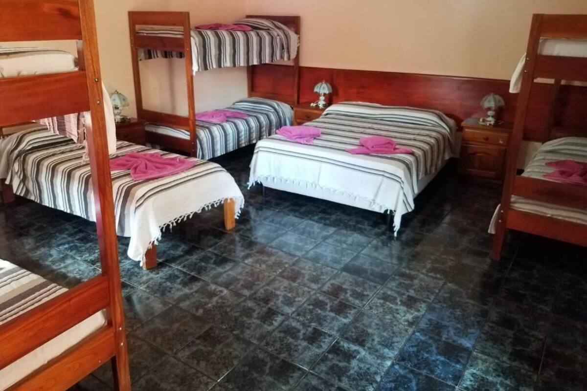 Une chambre avec quatre lits superposés, chacun doté de draps à rayures et de serviettes roses. La chambre a un sol carrelé et des têtes de lit en bois.