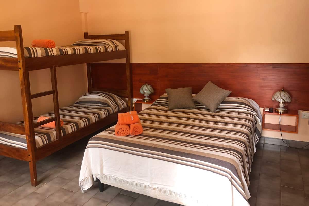 Une chambre avec des lits superposés, une table de chevet avec une lampe et une prise électrique au mur.