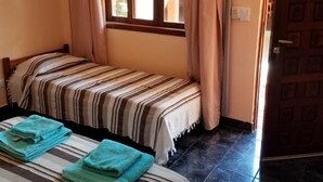 Une chambre avec deux lits, des rideaux beiges, un téléviseur à écran plat et un sol carrelé.