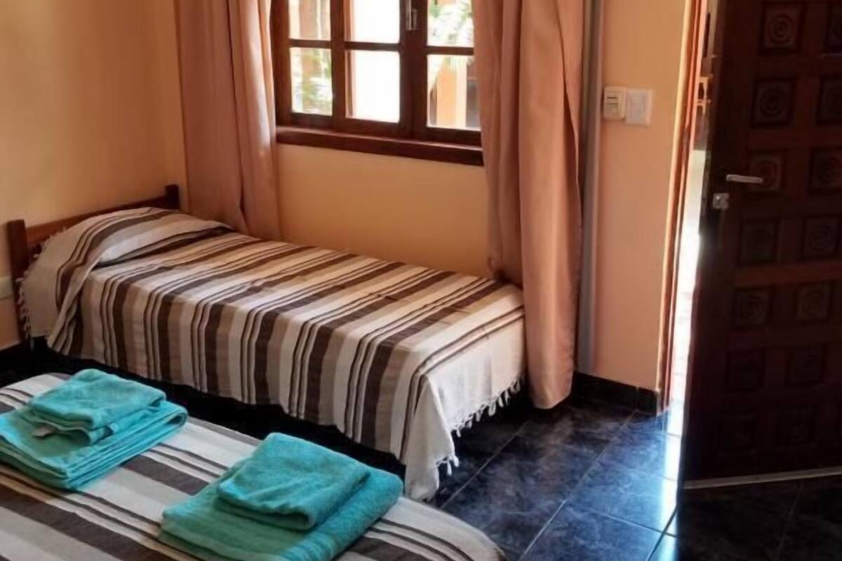 Une chambre avec deux lits, des rideaux beiges, un téléviseur à écran plat et un sol carrelé.