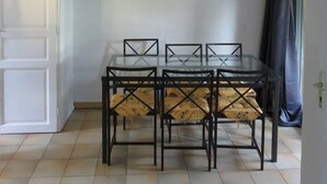 Un coin repas avec une table en verre et des chaises noires, un tableau au mur et une porte sur la gauche.