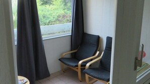 Une petite pièce bien éclairée, avec une fenêtre, deux chaises, une petite table et un sol carrelé.