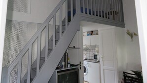 Un escalier menant à une chambre située en mezzanine, avec un espace cuisine en contrebas.