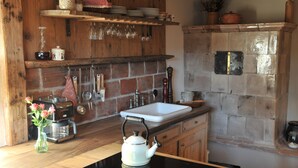 Una cocina con pared de ladrillo, estantes de madera, un lavamanos y una tetera sobre la encimera.