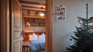 Un dormitorio acogedor con techo de madera, una cama con colcha a cuadros, una pequeña silla y un árbol de Navidad adornado.