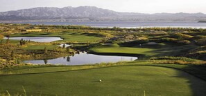 A golf course with water hazards, a flag, and mountains in the background.