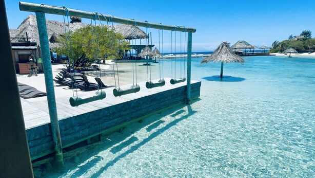 On peut clairement voir un salon de plage avec une terrasse en bois et des chaises longues, donnant sur une mer calme.