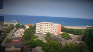 En bygning med flere etager og en parkeringsplads foran, beliggende tæt på en strand og et ocean.