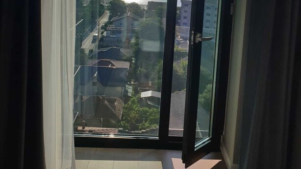 Et værelse med en stor skydedør, der fører ud til en balkon med udsigt over havet og omkringliggende bygninger.
