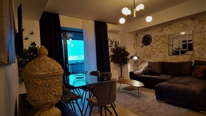 En moderne stue med en sofa, et spisebord med stole, en stor dekorativ vase, en potteplante og udsigt gennem en glasdør.
