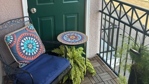 A green door with a crab painting, a blue chair with a colorful cushion, and a small round table with a patterned top. - Breezy Beach Retreat (Gulfport)