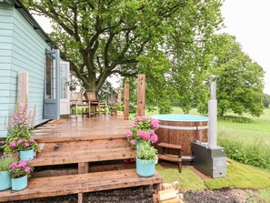 Terraza de madera con mobiliario exterior, jacuzzi y un gran árbol que da sombra.