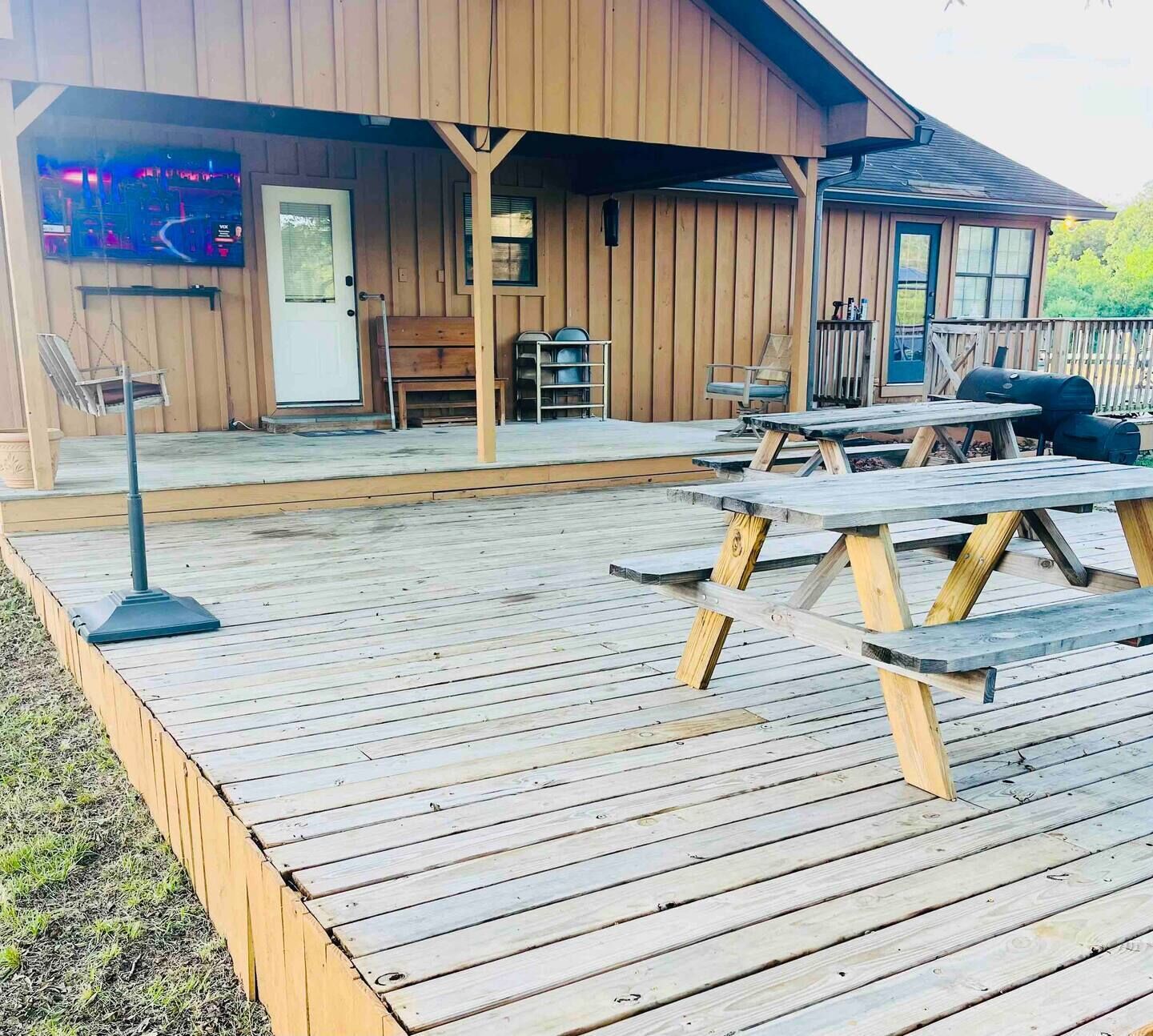 A wooden deck with picnic tables and a covered area with a door and windows.