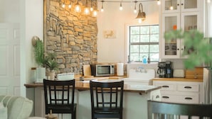 Una cocina con pared de piedra, armarios de madera, microondas, cafetera y luces colgantes.