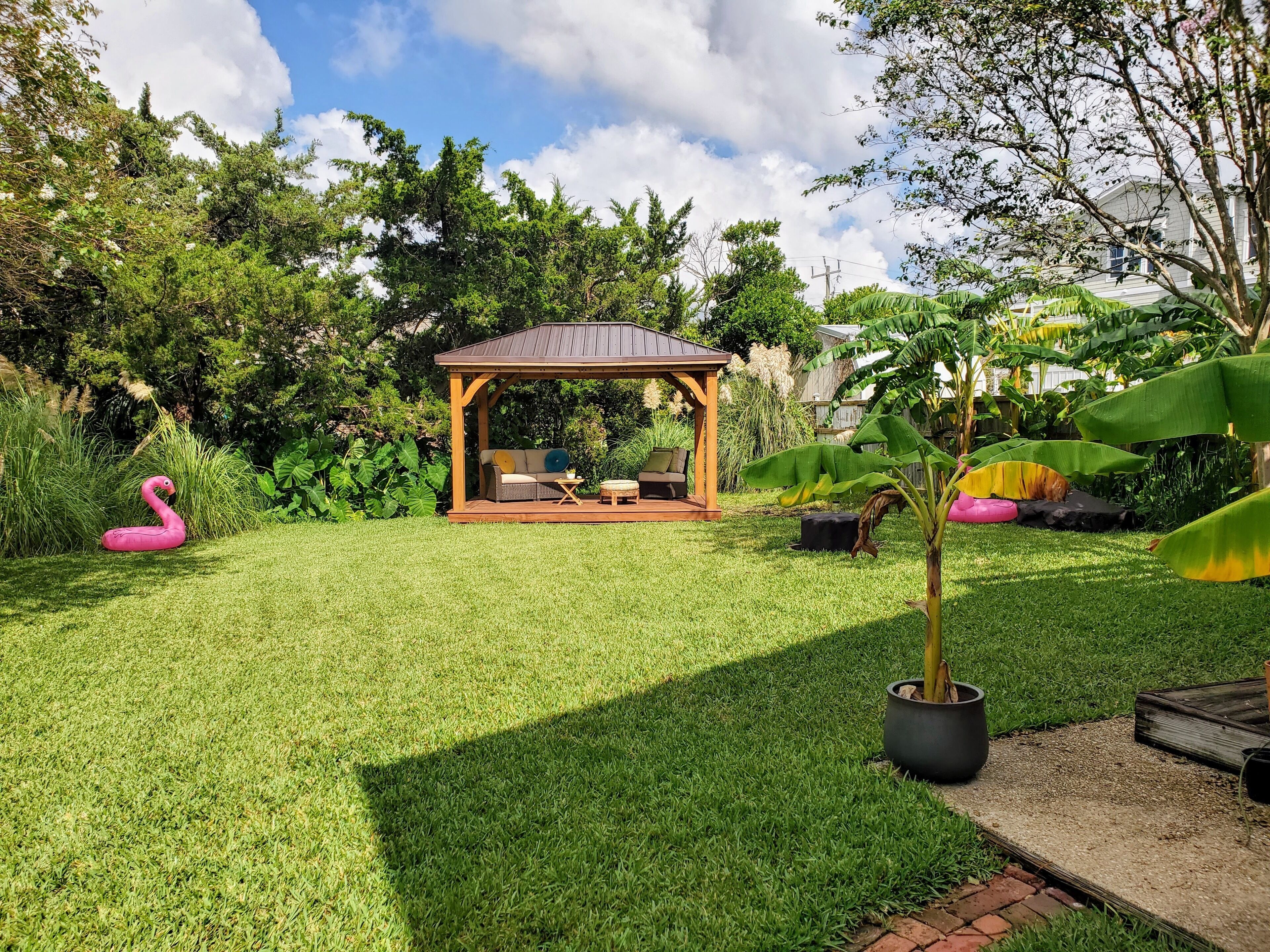 A well-maintained backyard with a wooden gazebo, a grassy lawn, and a potted plant.