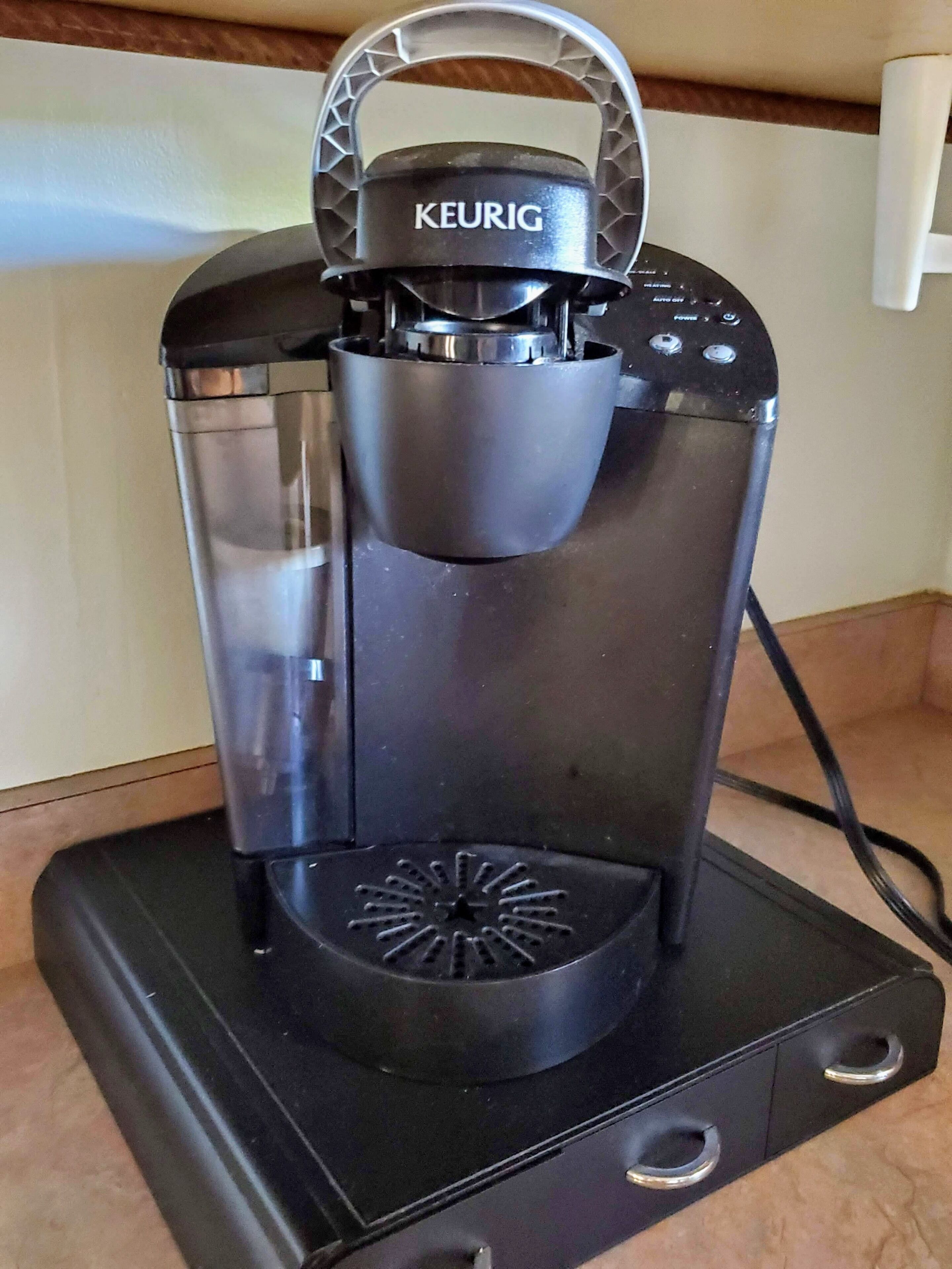 A Keurig coffee maker with a transparent water reservoir, a drip tray, and a control panel.