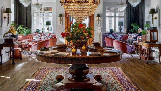 A luxurious living room with a grand chandelier, plush seating, and a central table with a vase of flowers. - Villa Brunnby (Nyhamnslage)