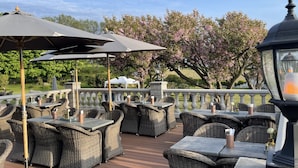 An outdoor patio with wicker furniture and umbrellas, a stone balustrade, and blooming trees in the background. - Villa Brunnby (Nyhamnslage)