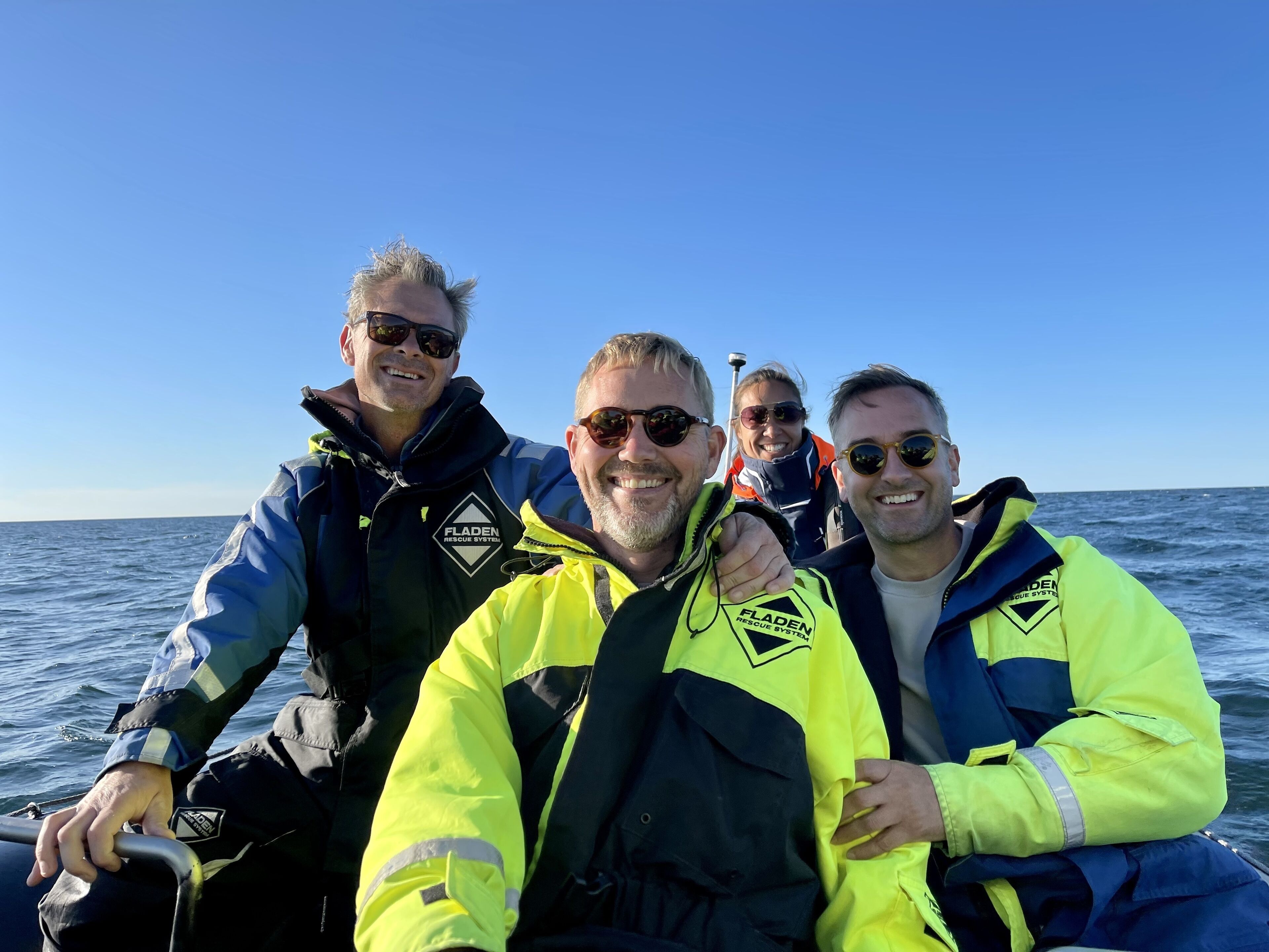 Fyra personer i en båt, alla bär flytvästar med en logotyp på.