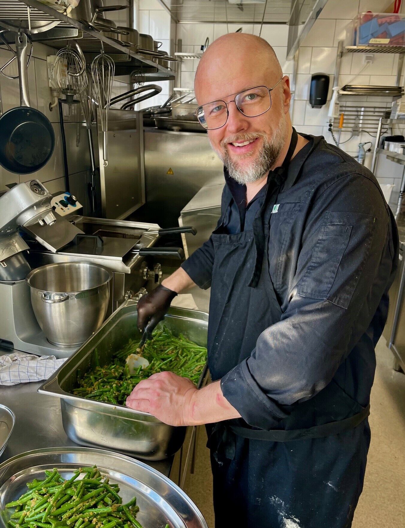 A chef preparing green beans in a commercial kitchen with stainless steel appliances and utensils.