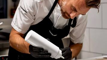 Un chef con camisa blanca y delantal negro preparando comida en una cocina.