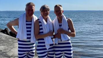 Three people standing on a concrete platform by the sea, wearing striped swimwear and white towels.