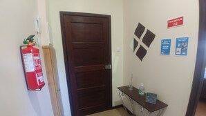 A hallway with a wooden door, a fire extinguisher, and emergency exit signs on the wall.