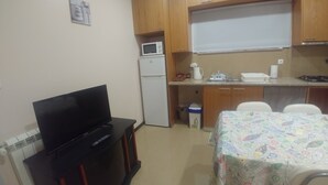 A compact kitchen with wooden cabinets, a microwave, a refrigerator, a sink, and a dining table with a colorful tablecloth.