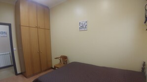 A bedroom with a bed, a wooden wardrobe, a chair, and a wall-mounted picture.