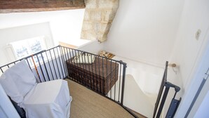 A high-ceilinged room with a sloped ceiling, a wooden beam, a white wall, a black metal railing, a covered sofa, and a small wooden table with a basket.