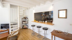 A modern kitchen with a wooden countertop, three bar stools, a wooden dining table, and a staircase with a white railing.