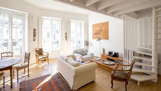 A spacious living room with a sofa, chairs, a dining table, and a bookshelf.