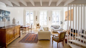 A spacious living room with a wooden floor, a sofa, a coffee table, and a dining area with chairs and a table.