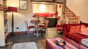 A cozy living room with a red sofa, a glass coffee table, and a fireplace. There is a kitchen area with a red countertop and a wooden staircase. - The Curious Orange (Windermere)