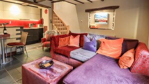 A living room with a red and purple sofa, a glass coffee table, and a kitchen in the background. - The Curious Orange (Windermere)