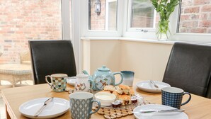 A dining table set with plates, mugs, a teapot, and biscuits. - Claire Cottage (Selby)