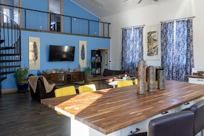A spacious living area with a wooden dining table, yellow chairs, a black sofa, and a TV mounted on the wall. - You have to see it! (Davenport)