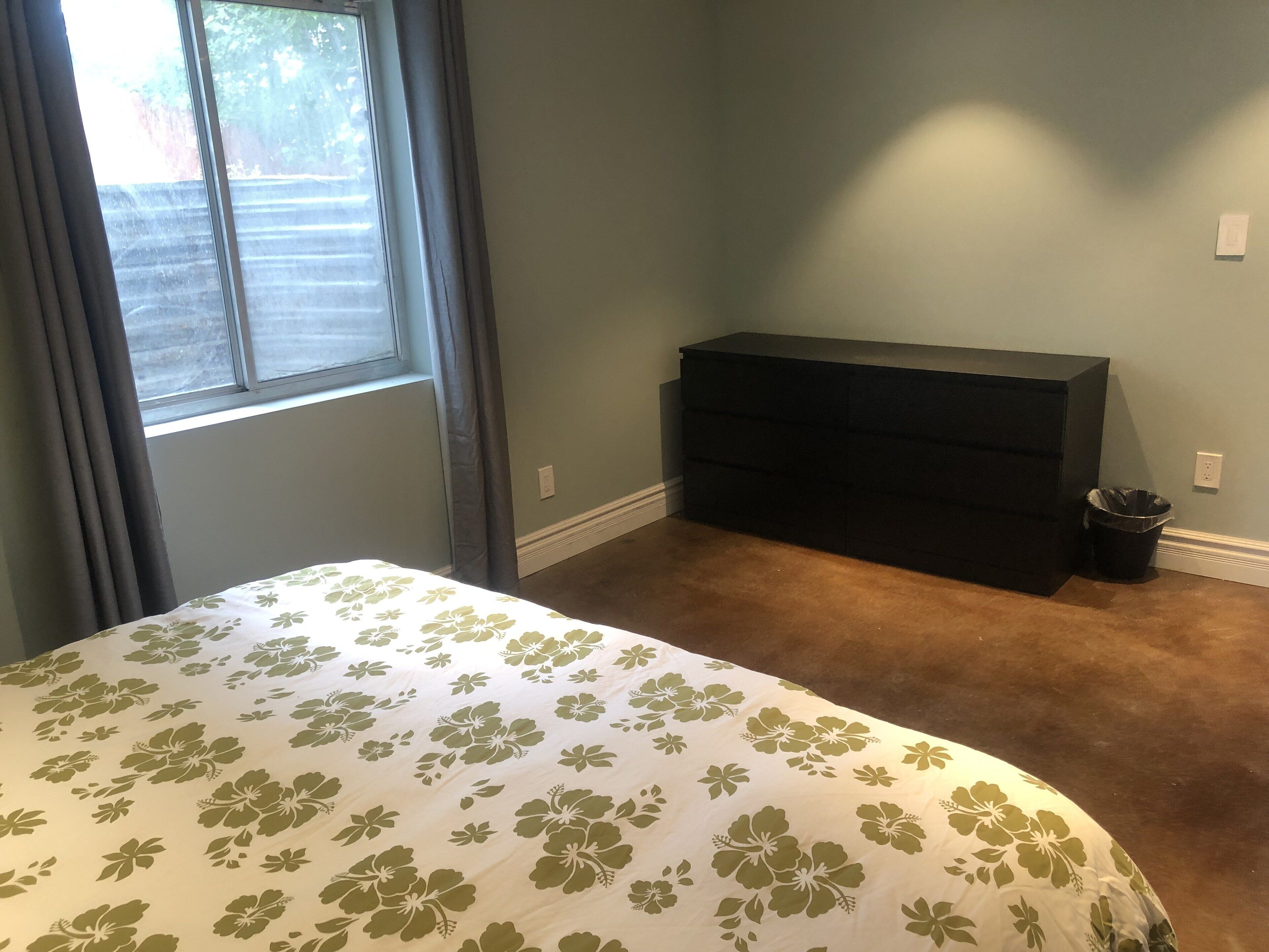A bedroom with a bed, a dresser, and a window with curtains.