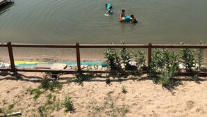 Un lac avec des maisons en arrière-plan, une plage de sable et une clôture.