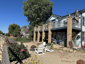 A two-story house with a balcony, a hammock, and a garden area with flowers and a fire pit. - Lakefront, Beach, Fishing, Hot Tub, Gated, Fire Pit (Denver)