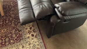 Un salon avec un canapé en cuir noir, un tapis à motifs et une petite table en bois.