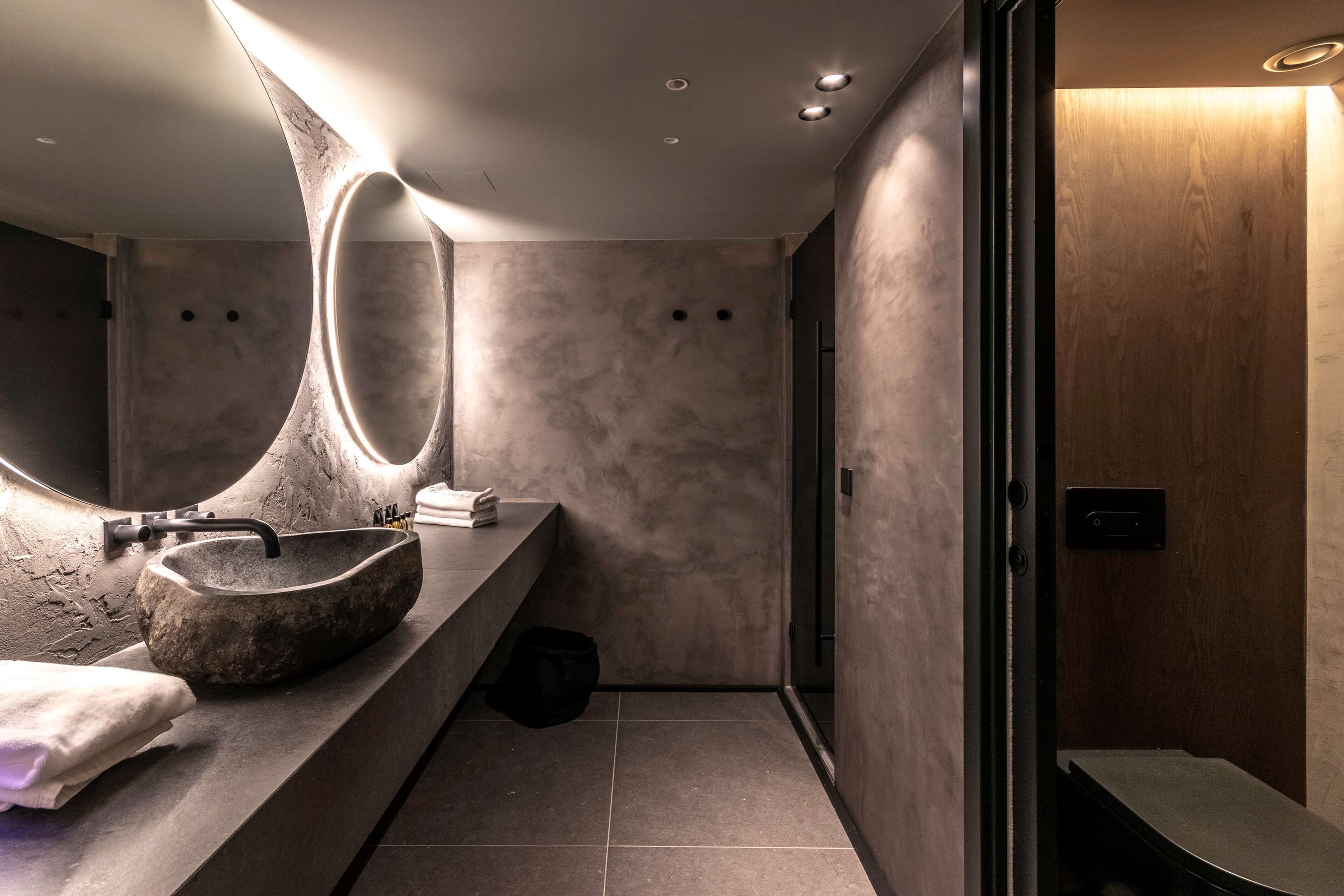 Un baño moderno con un espejo ovalado grande, un lavamanos de piedra y un perchero para toallas.