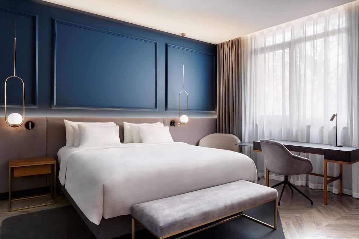A modern hotel room with a large bed, bedside tables, a desk, and a chair.