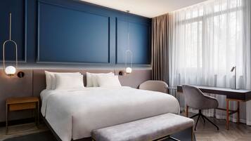 A modern hotel room with a large bed, bedside tables, a desk, and a chair.