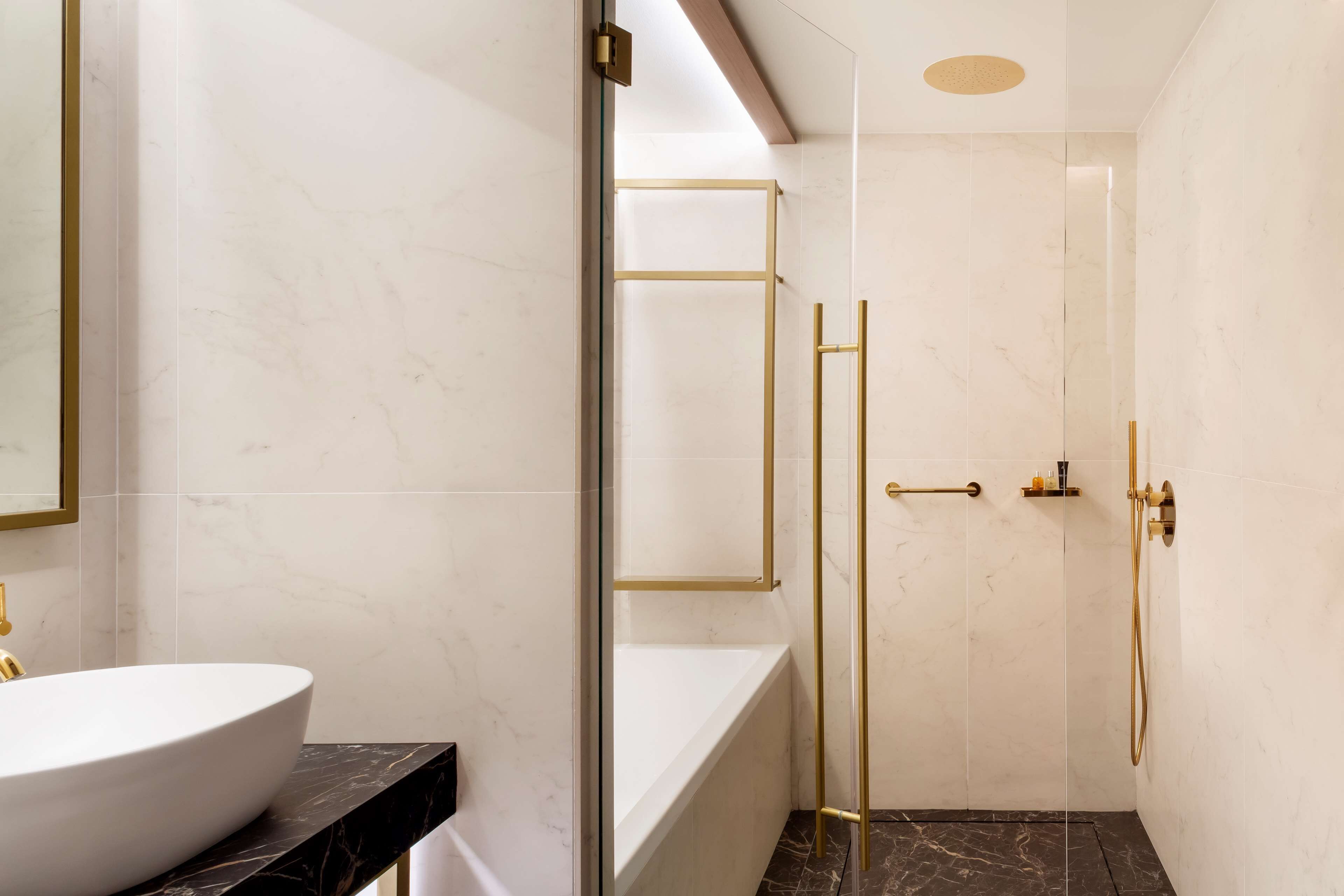 Un baño moderno con un lavamanos de mármol blanco, ducha con cerramiento de vidrio y detalles dorados.