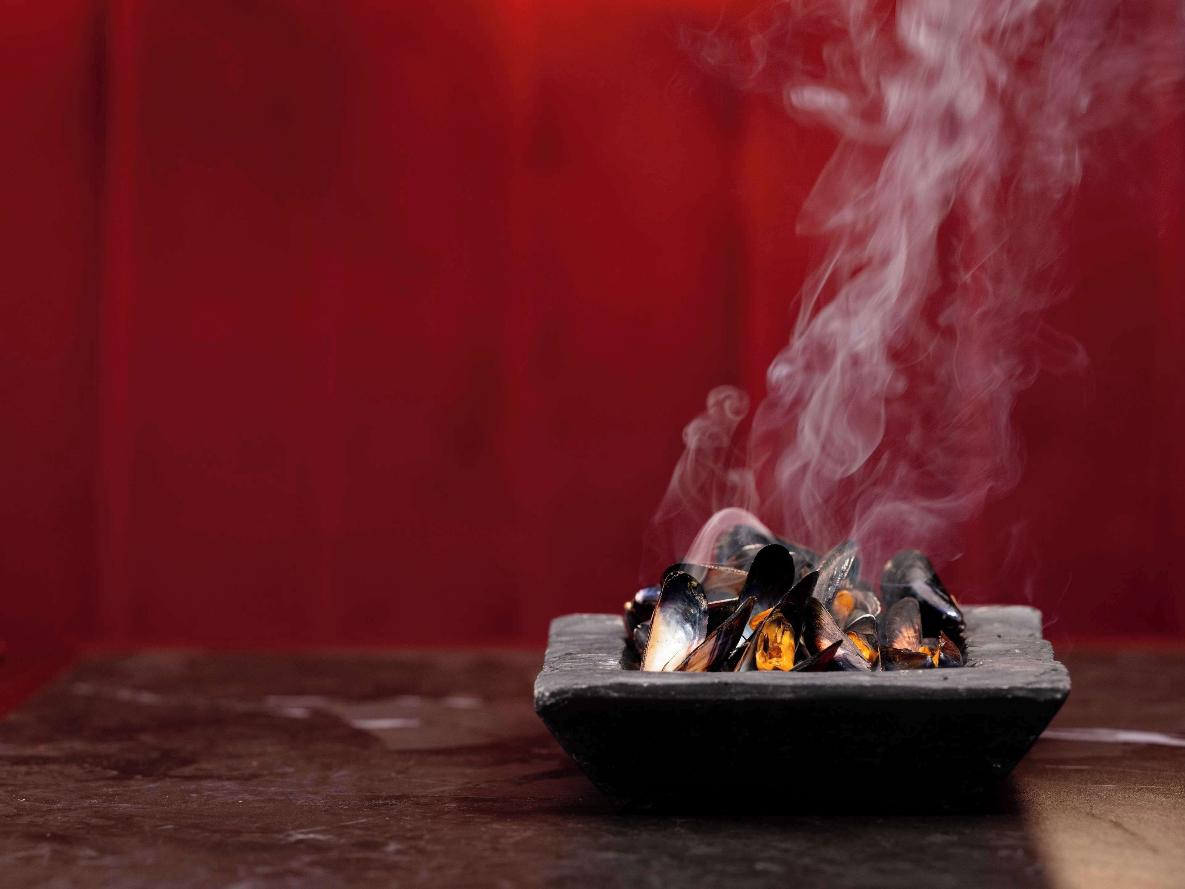 A dish of mussels being cooked with steam rising from them.