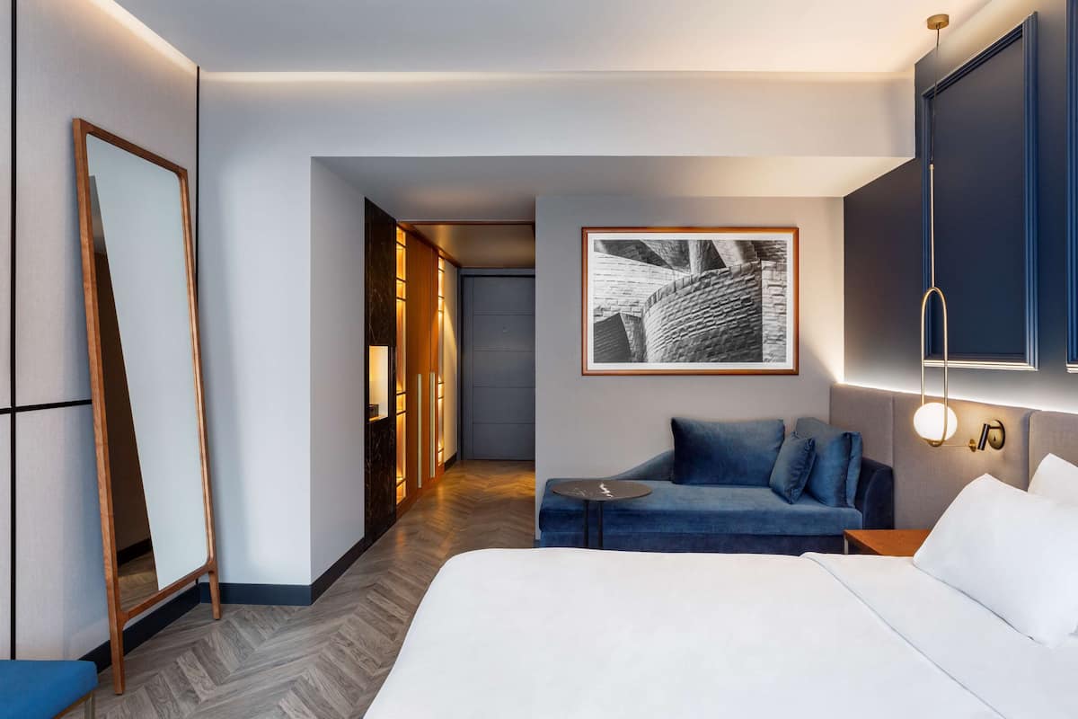 A modern hotel room with a large bed, a blue sofa, a small table, and a wardrobe.