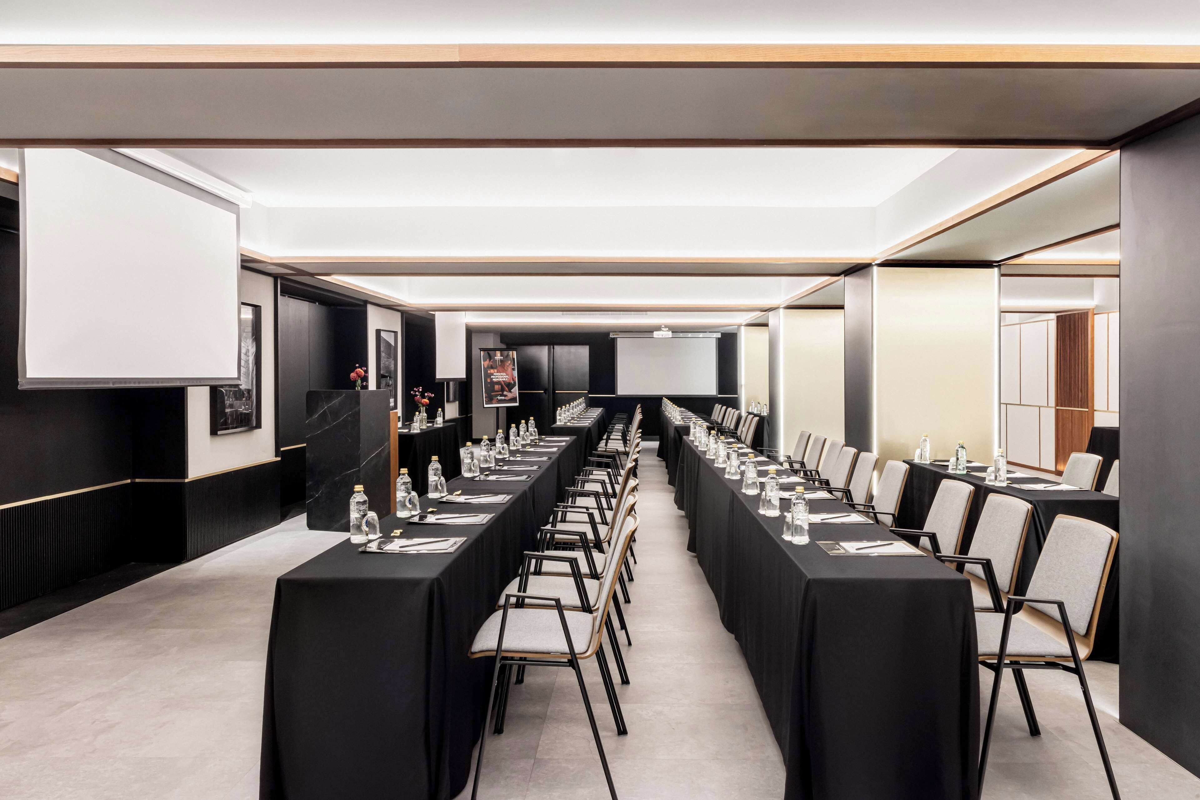 Un salón de conferencias con mesas largas, sillas y una pantalla de proyector.