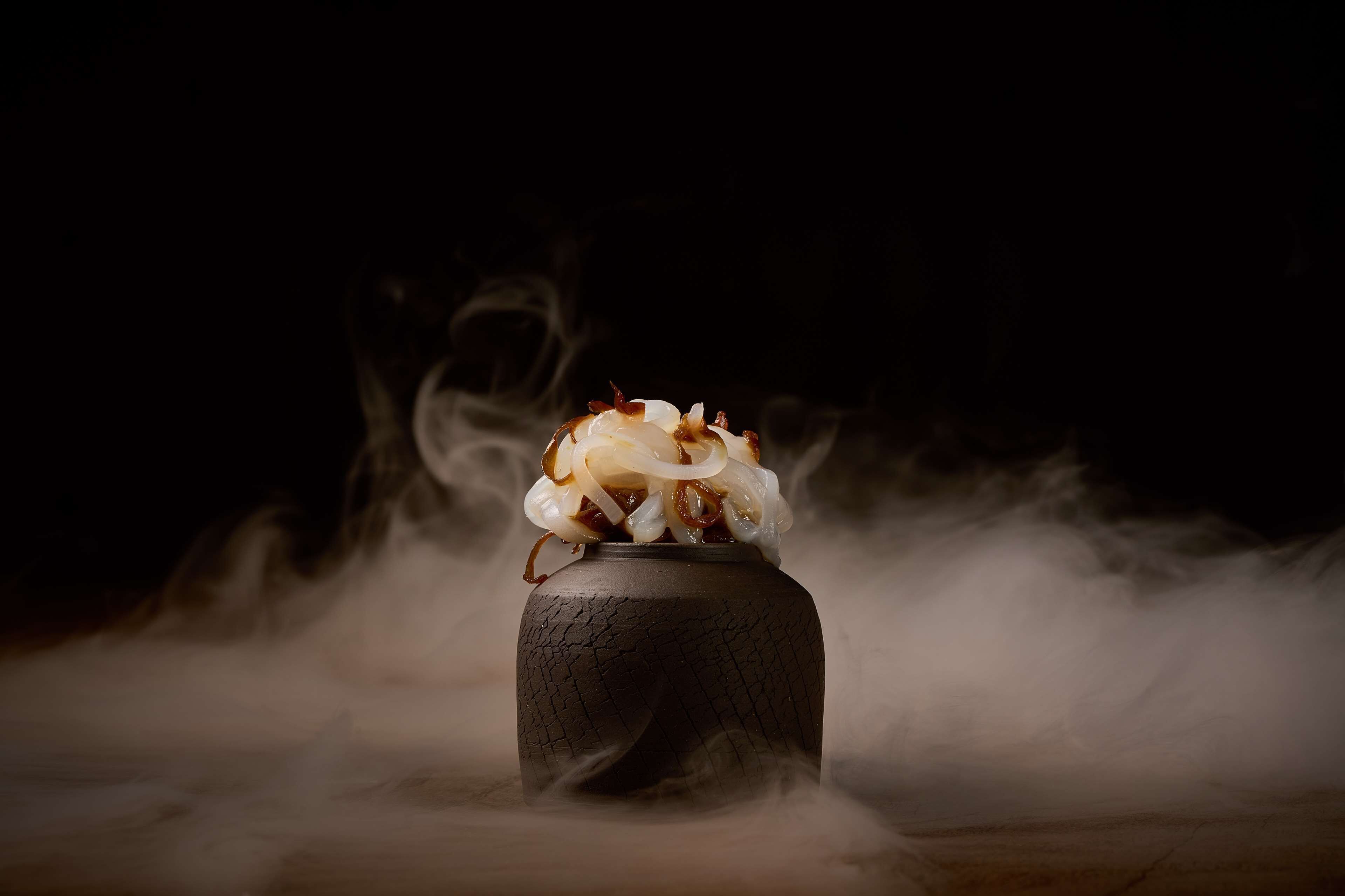 A pot with a steaming mixture of onions and spices, surrounded by smoke.