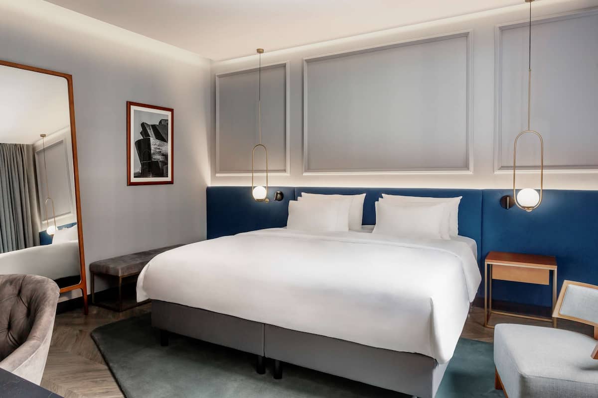 A modern hotel room with a large bed, bedside tables, a chair, and a mirror.